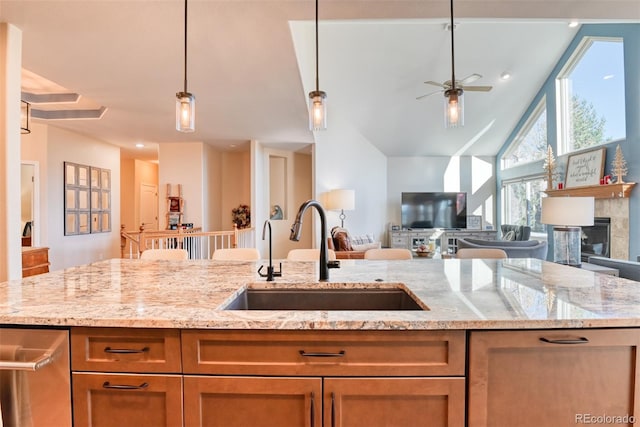 kitchen with pendant lighting, ceiling fan, light stone counters, and sink