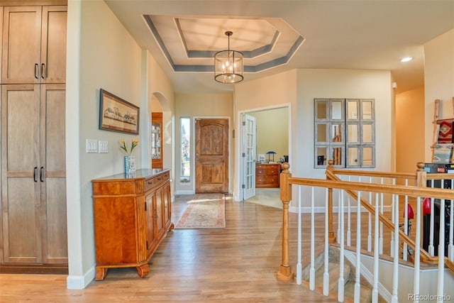 foyer with a tray ceiling, a chandelier, and light hardwood / wood-style floors