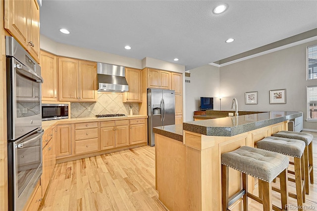 14878 E Aberdeen Ave, Centennial, CO 80016 - kitchen with stainless steel appliances, light brown cabinets, wall chimney exhaust hood, a breakfast bar, and recessed lighting