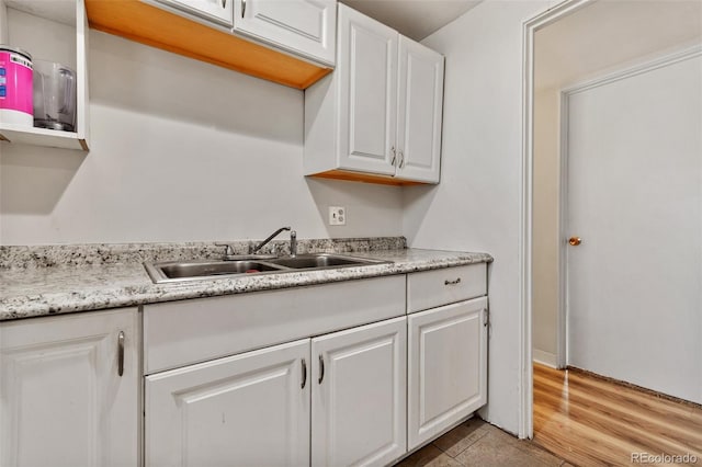 kitchen with white cabinetry, light hardwood / wood-style floors, light stone countertops, and sink