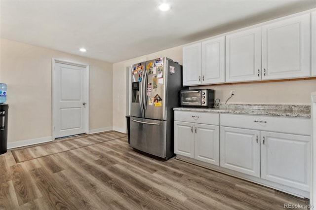 kitchen with light hardwood / wood-style floors, white cabinetry, light stone counters, and stainless steel fridge with ice dispenser