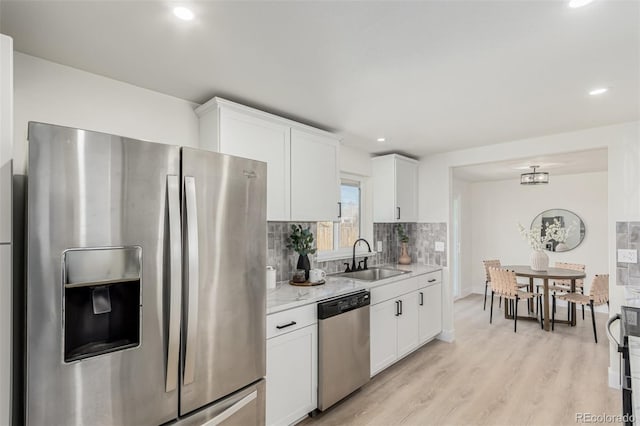 kitchen with light wood finished floors, stainless steel appliances, backsplash, white cabinetry, and a sink