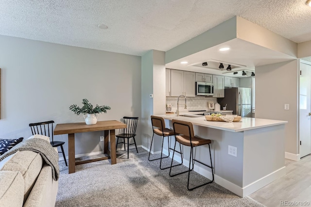 kitchen with gray cabinetry, stainless steel appliances, sink, kitchen peninsula, and a textured ceiling