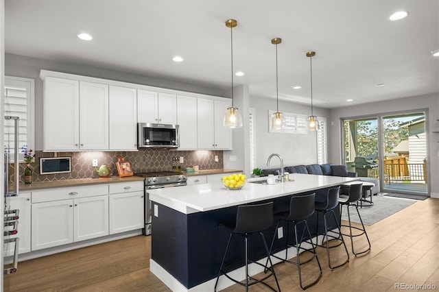 4535 W 50th Ave, Denver, CO 80212 - kitchen featuring appliances with stainless steel finishes, a sink, wood finished floors, tasteful backsplash, and an island with sink