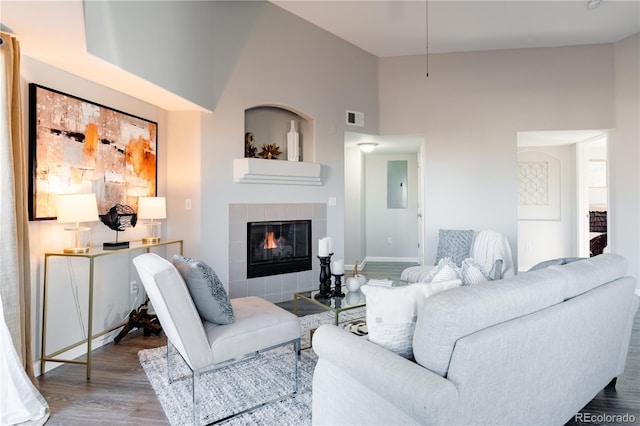 living room with hardwood / wood-style flooring, electric panel, a high ceiling, a wall mounted air conditioner, and a fireplace