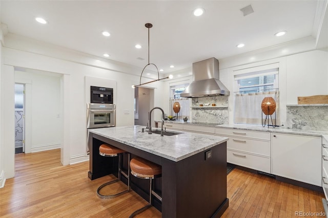 kitchen with white cabinets, tasteful backsplash, an island with sink, sink, and ventilation hood