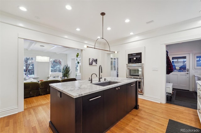 kitchen featuring light hardwood / wood-style floors, hanging light fixtures, sink, dark brown cabinetry, and an island with sink