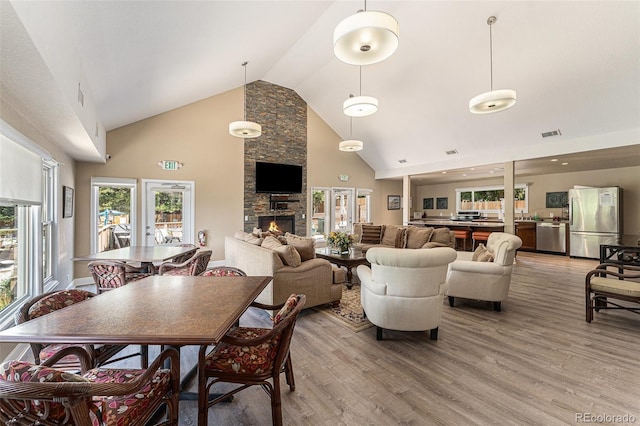 dining area featuring wood-type flooring, a stone fireplace, high vaulted ceiling, and french doors