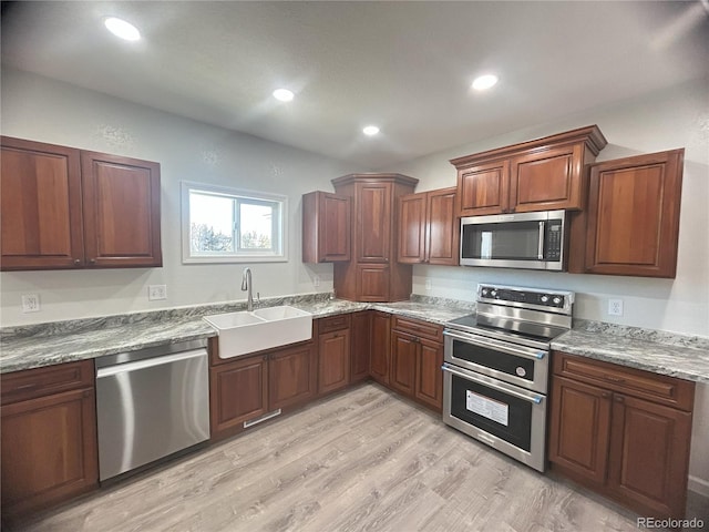 kitchen with sink, stainless steel appliances, light stone counters, and light hardwood / wood-style floors