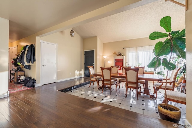 dining space with a textured ceiling, hardwood / wood-style floors, baseboards, and vaulted ceiling