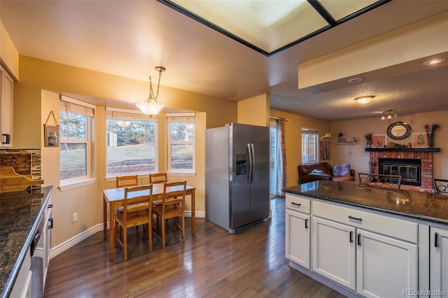 kitchen with dark wood-style floors, plenty of natural light, a fireplace, stainless steel fridge with ice dispenser, and open floor plan