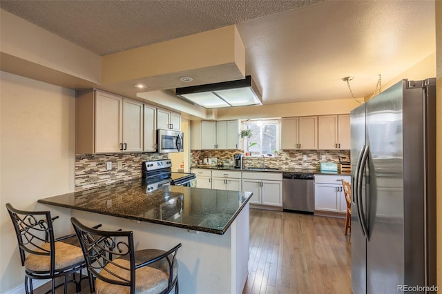 kitchen featuring a peninsula, a sink, decorative backsplash, stainless steel appliances, and light wood-style floors