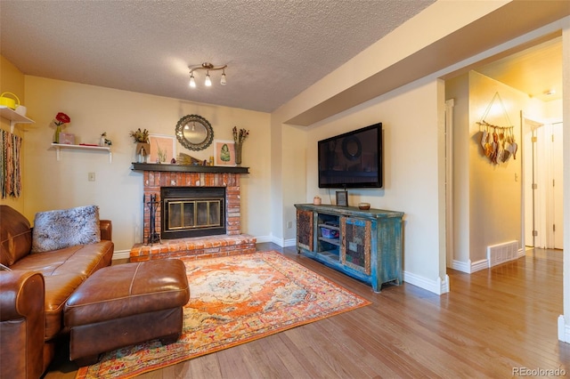 living area with visible vents, a brick fireplace, baseboards, wood finished floors, and a textured ceiling