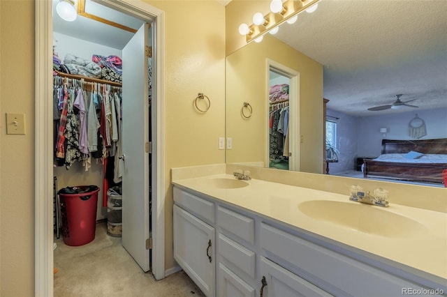 bathroom with double vanity, a textured ceiling, a walk in closet, and a sink