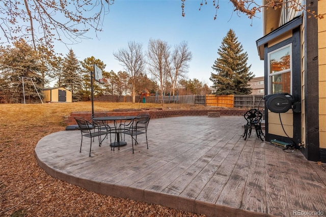 view of patio / terrace featuring an outbuilding, a wooden deck, outdoor dining area, a fenced backyard, and a storage shed