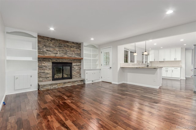 5890 W Quarles Dr, Littleton, CO 80128 - unfurnished living room featuring dark wood-style flooring, built in shelves, a stone fireplace, baseboards, and recessed lighting