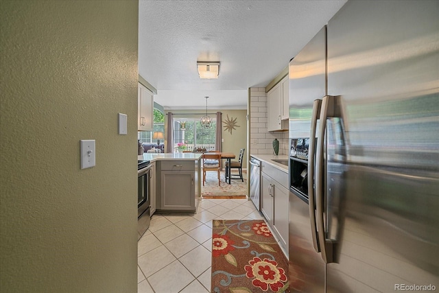 10389 W Fair Ave Unit E, Littleton, CO 80127 - kitchen with appliances with stainless steel finishes, a textured wall, light countertops, light tile patterned floors, and a peninsula