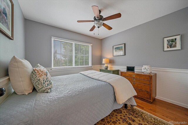 10389 W Fair Ave Unit E, Littleton, CO 80127 - bedroom with wood finished floors, a ceiling fan, baseboards, and a wainscoted wall