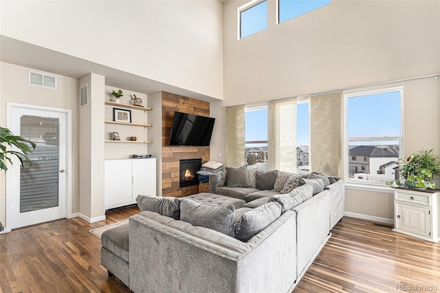 living room with a fireplace, visible vents, baseboards, and wood finished floors