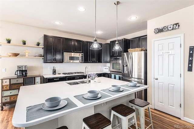 kitchen with light wood-style floors, pendant lighting, a kitchen breakfast bar, appliances with stainless steel finishes, and a sink