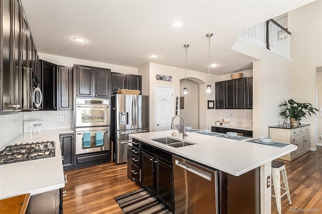 kitchen featuring appliances with stainless steel finishes, light countertops, a sink, decorative backsplash, and dark wood-style floors