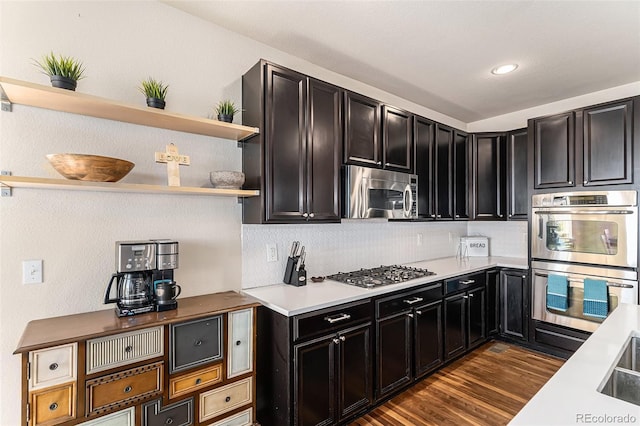 kitchen with dark cabinets, dark wood-style flooring, light countertops, open shelves, and appliances with stainless steel finishes
