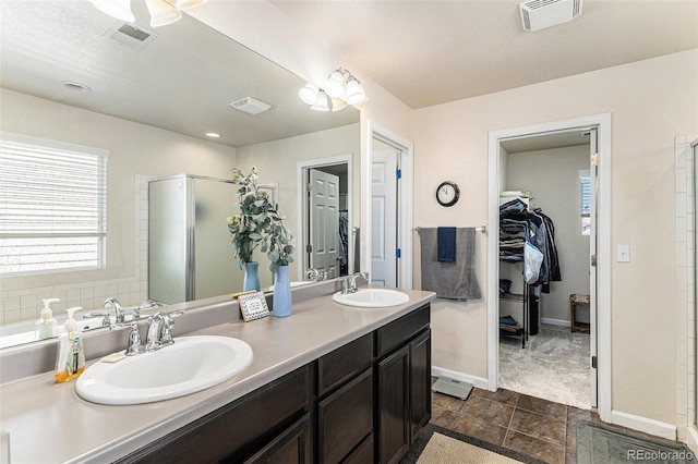 bathroom with a shower stall, double vanity, a sink, and visible vents