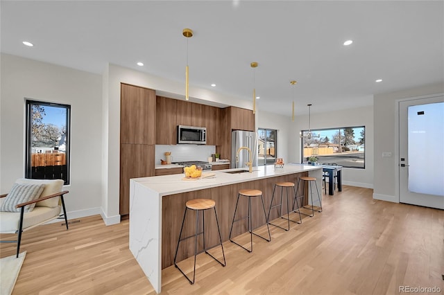 kitchen with brown cabinets, a breakfast bar area, stainless steel appliances, a sink, and modern cabinets