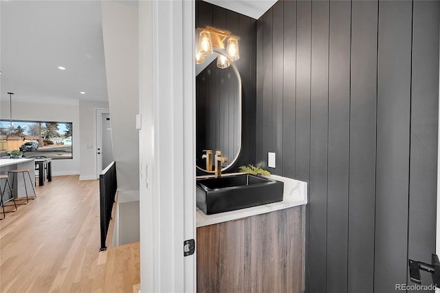 interior space with wood walls, a sink, baseboards, hanging light fixtures, and light wood-type flooring