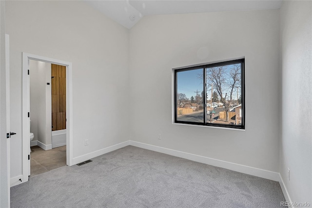 carpeted empty room with baseboards, visible vents, and vaulted ceiling