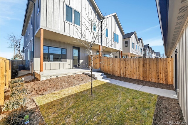 back of property with board and batten siding, a patio area, a fenced backyard, and a lawn