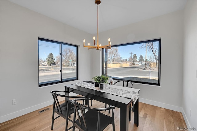 dining space featuring baseboards, visible vents, a notable chandelier, and light wood finished floors