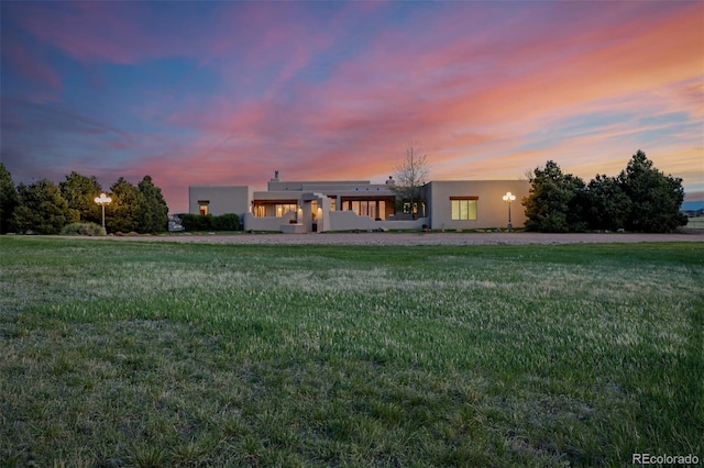 back of property at dusk featuring stucco siding and a yard