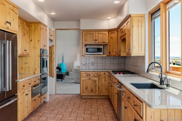 kitchen with appliances with stainless steel finishes, a sink, decorative backsplash, light stone countertops, and a warming drawer