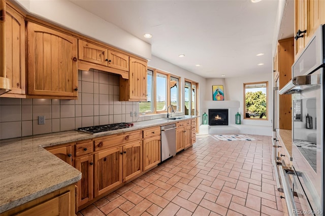 kitchen with stainless steel appliances, a sink, backsplash, a lit fireplace, and brick patterned floors