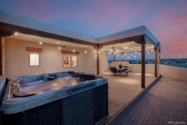 deck at dusk with a hot tub and outdoor dining space