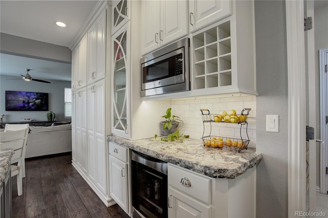 kitchen featuring white cabinetry, stainless steel microwave, open floor plan, decorative backsplash, and wine cooler