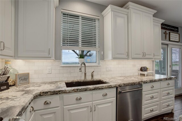 kitchen with stainless steel dishwasher, a sink, white cabinets, and tasteful backsplash