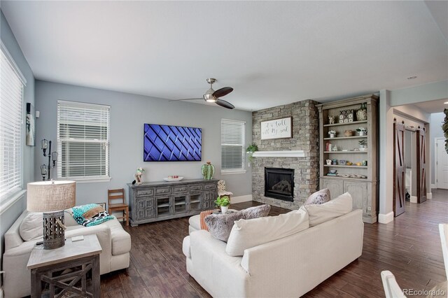 living room featuring baseboards, ceiling fan, dark wood-style floors, and a stone fireplace