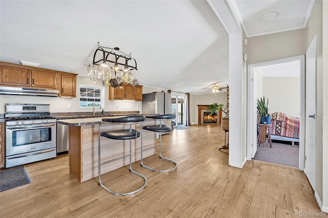 5856 John Ross Ct, Peyton, CO 80831 - kitchen featuring stainless steel gas stove, under cabinet range hood, a kitchen island, a textured ceiling, and brown cabinetry