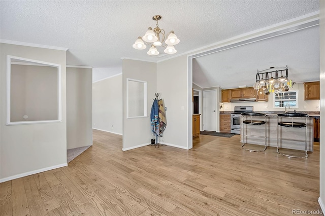 5856 John Ross Ct, Peyton, CO 80831 - kitchen with stainless steel gas stove, brown cabinetry, a chandelier, light wood-style floors, and under cabinet range hood