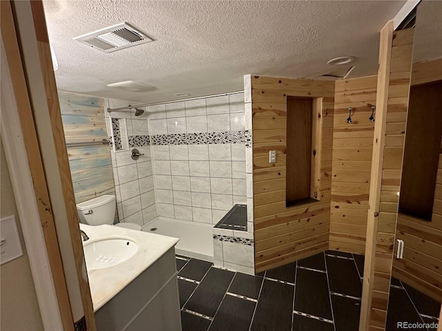 full bathroom featuring visible vents, wood walls, a stall shower, a textured ceiling, and vanity