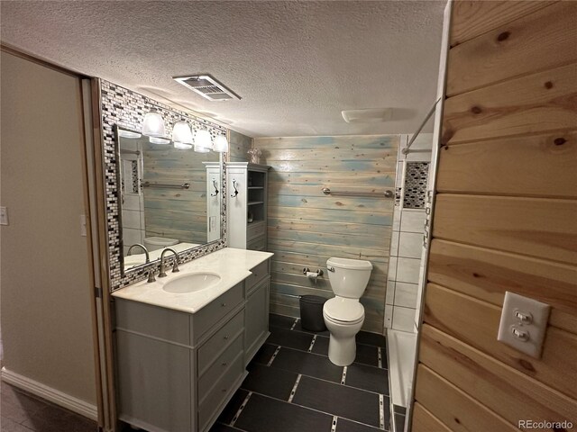 bathroom featuring a textured ceiling, vanity, toilet, and wooden walls