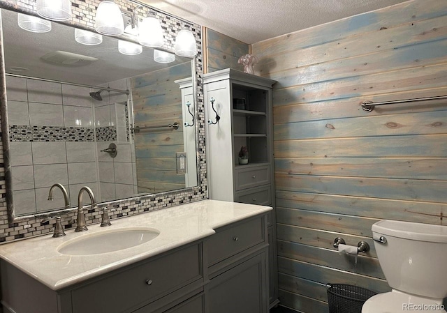 bathroom with toilet, a textured ceiling, a tile shower, decorative backsplash, and vanity