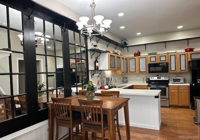 kitchen featuring an inviting chandelier, black appliances, sink, hardwood / wood-style flooring, and kitchen peninsula