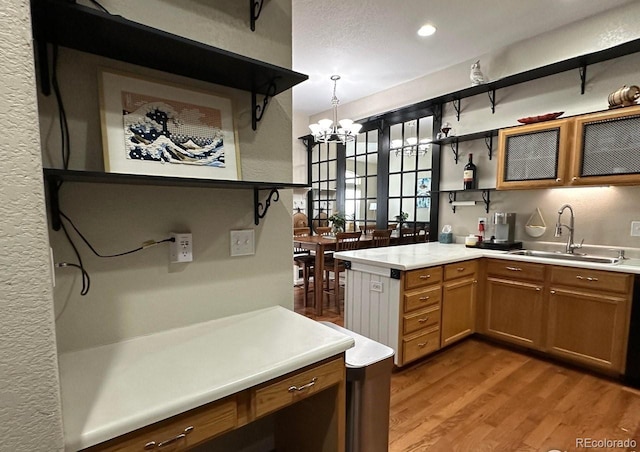 kitchen with kitchen peninsula, sink, decorative light fixtures, a chandelier, and light hardwood / wood-style floors