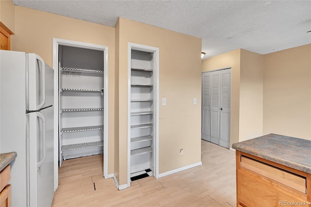 interior space with light brown cabinetry, white fridge, a textured ceiling, and light wood-type flooring