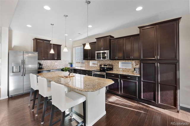 4875 S Catawba St, Aurora, CO 80016 - kitchen with stainless steel appliances, dark brown cabinetry, a kitchen island, backsplash, and a breakfast bar area