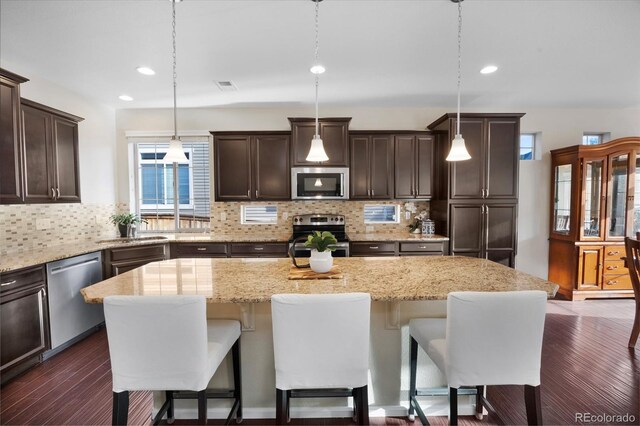4875 S Catawba St, Aurora, CO 80016 - kitchen with appliances with stainless steel finishes, dark brown cabinets, a kitchen island, a breakfast bar, and recessed lighting