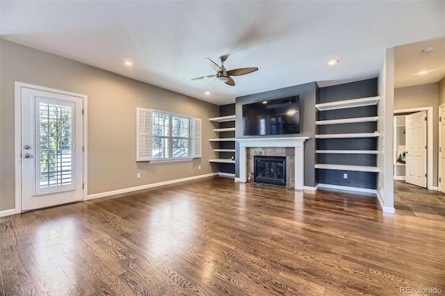 unfurnished living room with built in shelves, ceiling fan, dark hardwood / wood-style flooring, and a tiled fireplace